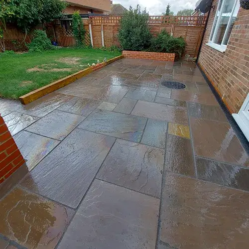 A patio with a brick wall and grass.